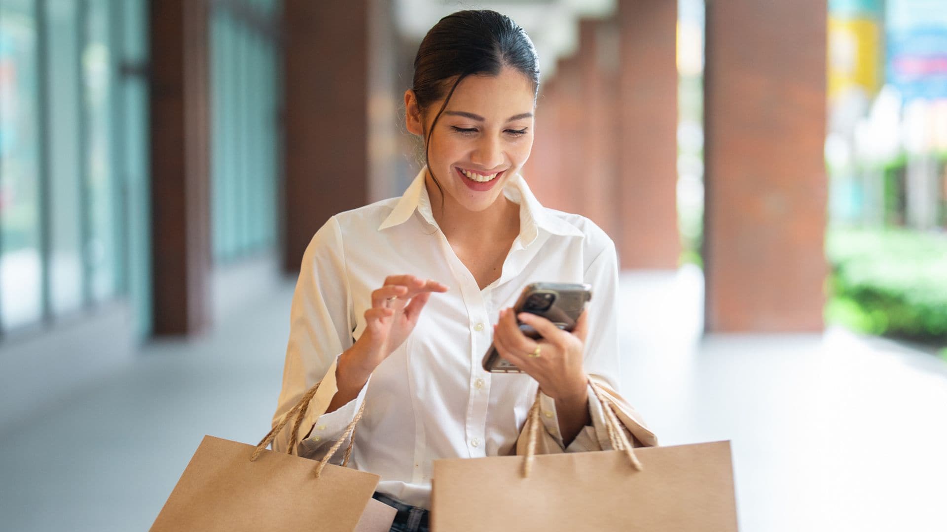 Mujer con bolsas de compras sonriente mirando su teléfono móvil