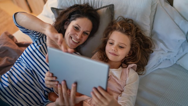 Una madre y una hija viendo una tablet en la cama