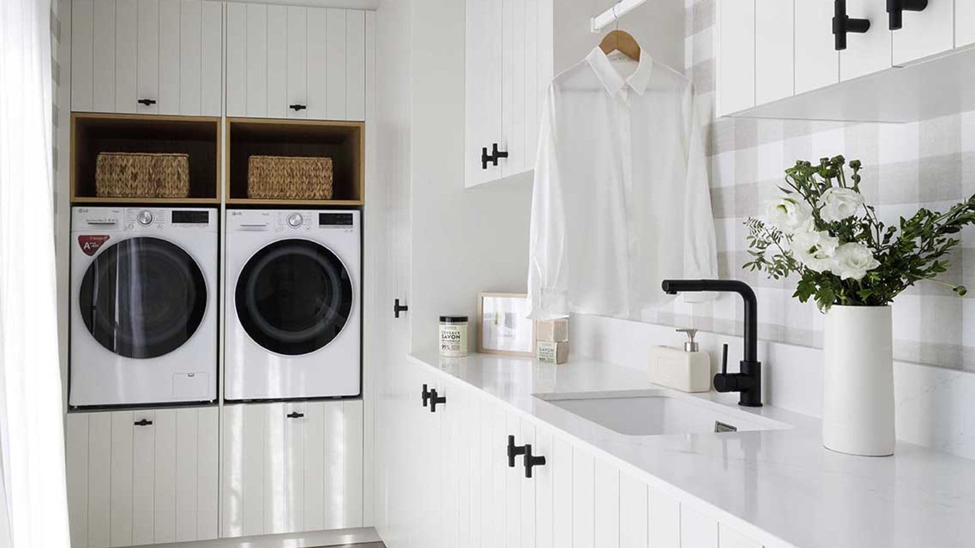 Lavadero con muebles blancos de lamas, lavadora y secadora en alto, fregadero, cestos, jarrón