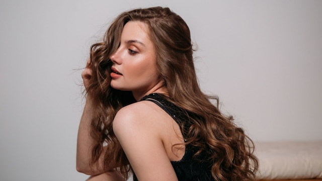 Rostro de mujer mirando de lado mientras se toca el cabello largo y ondulado