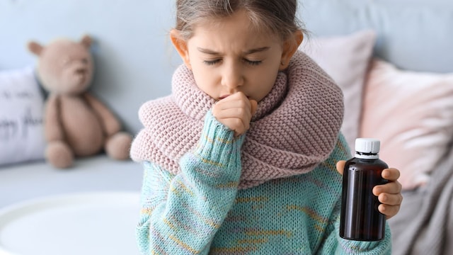 Niña tosiendo con un frasco de jarabe en la mano