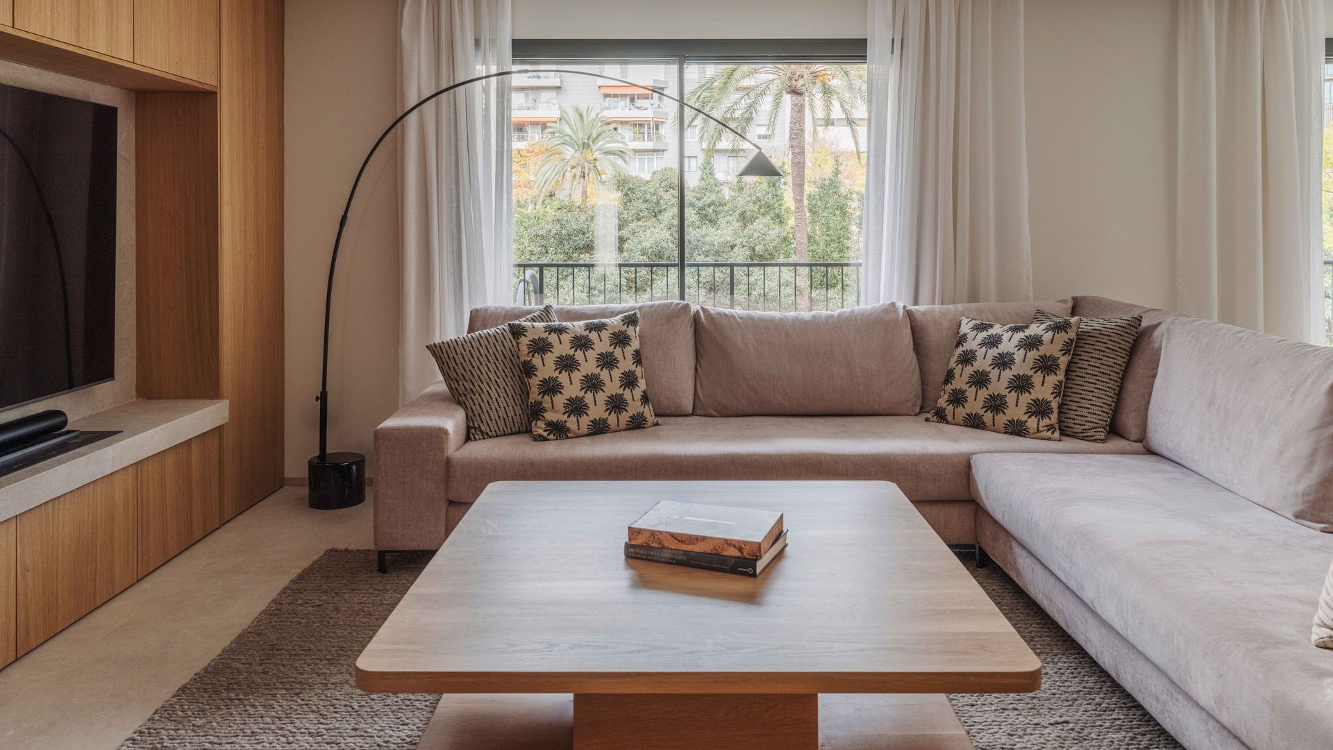 Salón con mueble de televisión de madera, sofás beiges, lámpara de pie, cortinas blancas 
