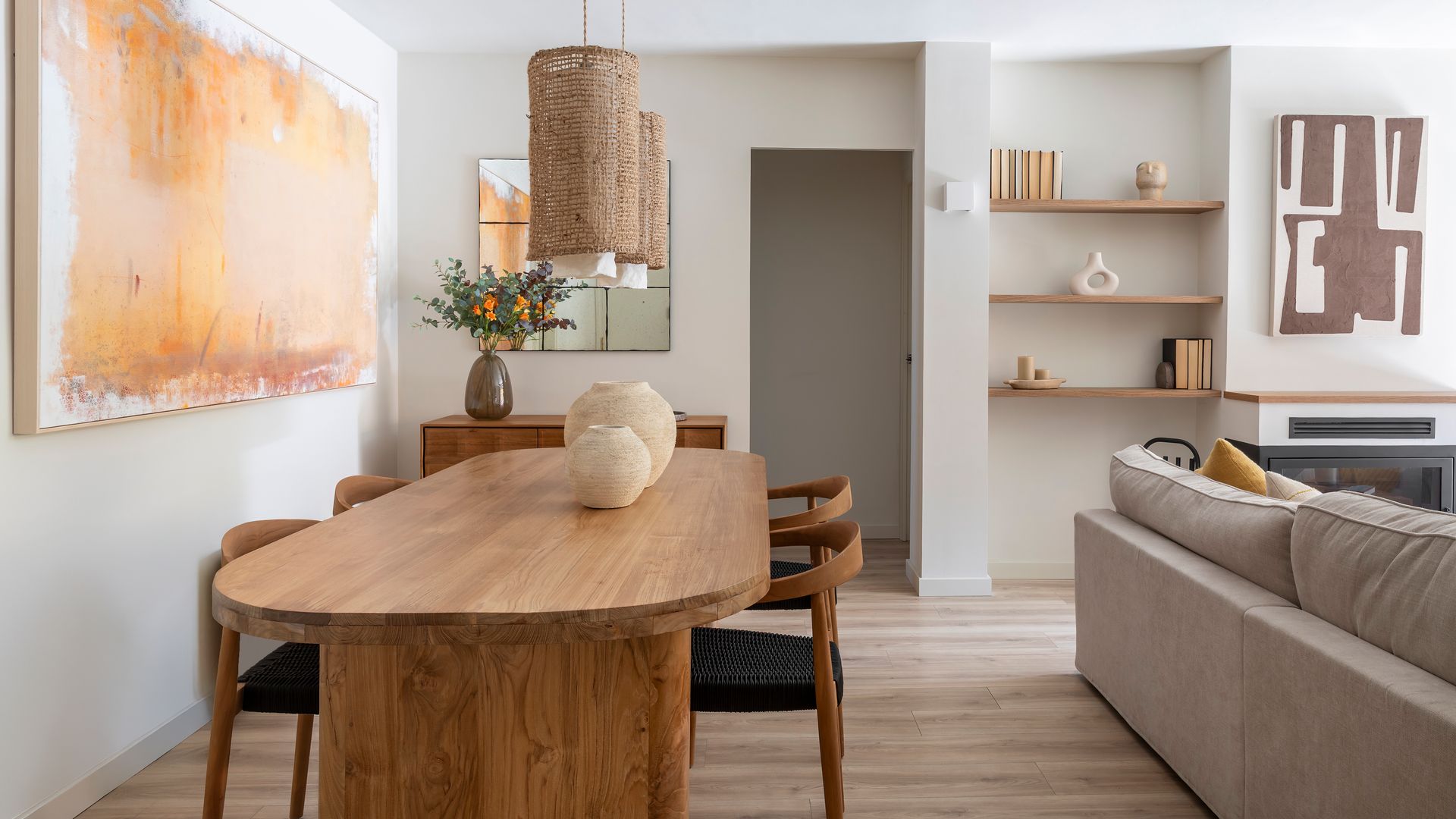 Salón comedor en tonos neutros, mesa de madera, hornacina con baldas, cuadro en la pared, lámparas de techo de fibras vegetales 