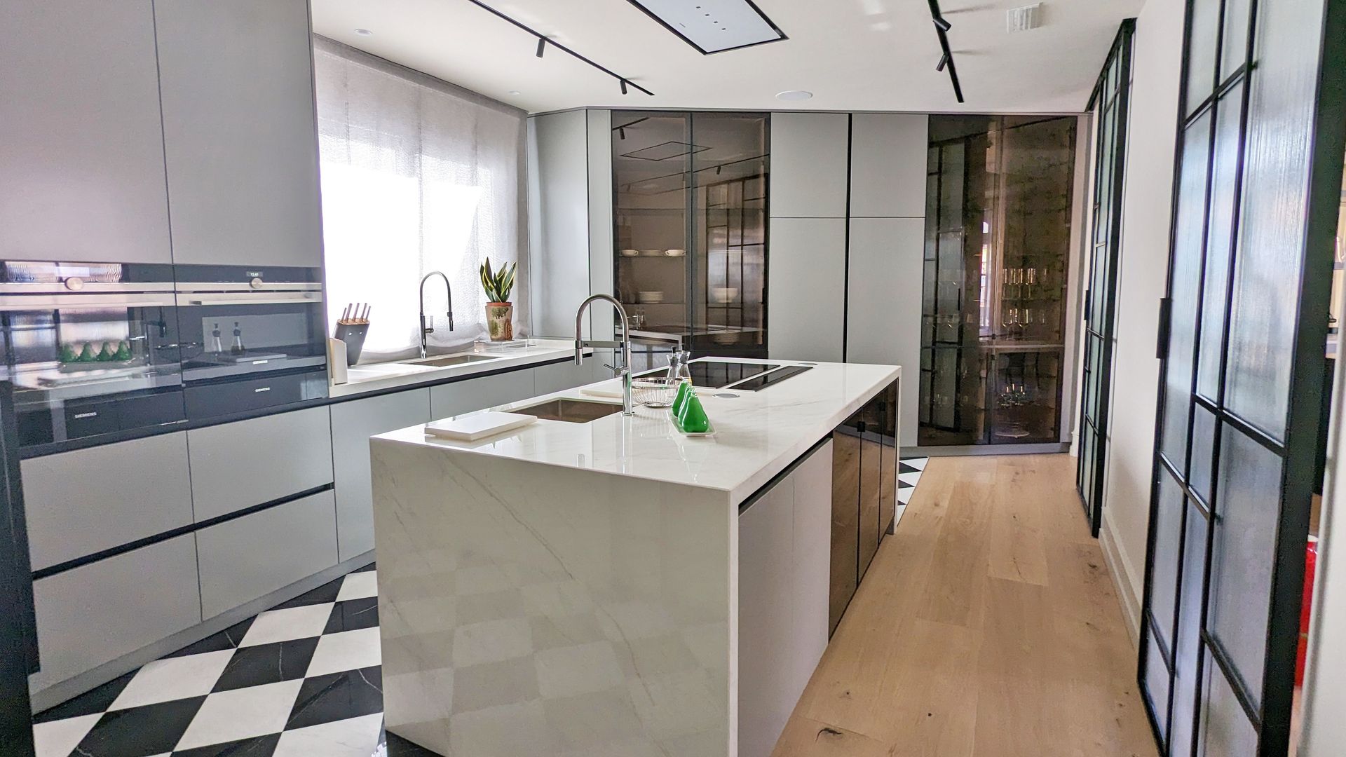 Cocina con isla central, suelo de madera, armarios vitrina, muebles grises