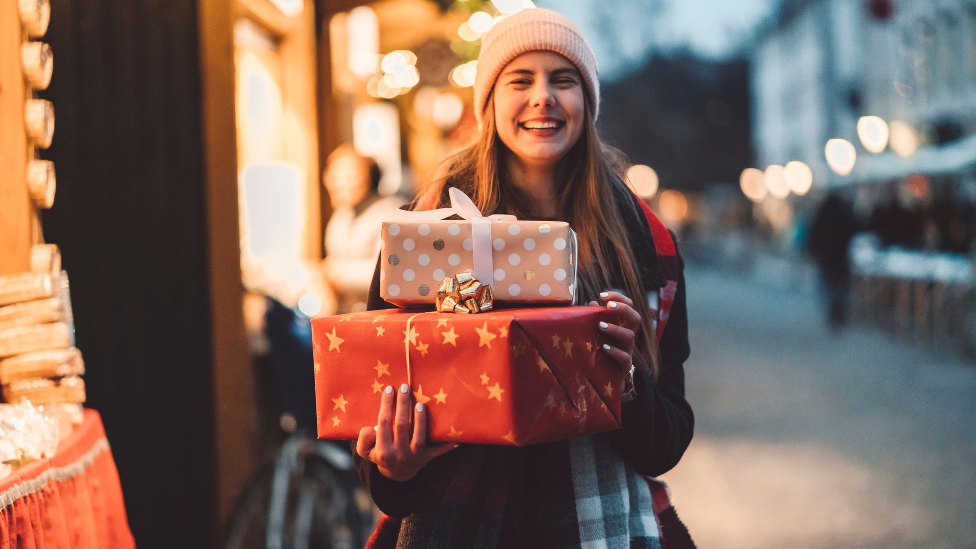 Chica feliz con regalos de Navidad en paquetes, sonriendo por la calle nevada y decorada.