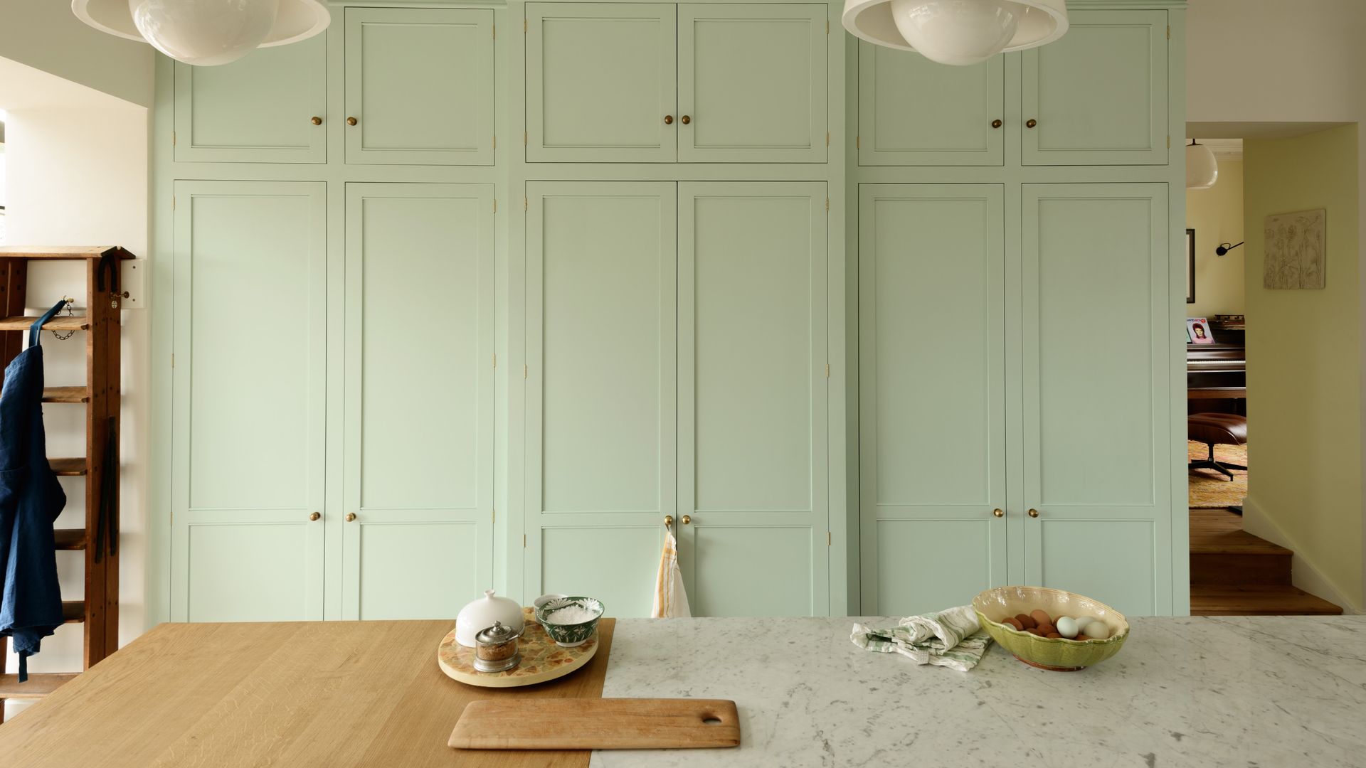 Cocina con armario verde claro, encimera de mármol con mesa de madera adosada