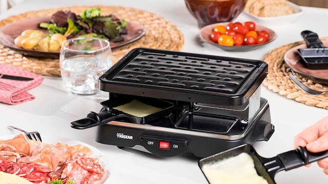 Una parrilla eléctrica en una mesa con más platos y comida