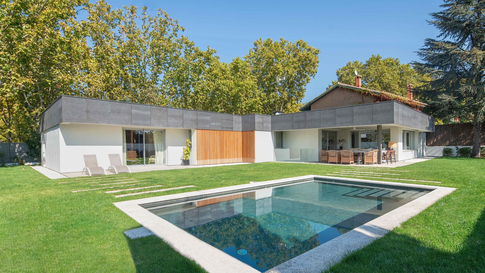 Casa con piscina y jardín, con lamas de madera, tumbonas y césped