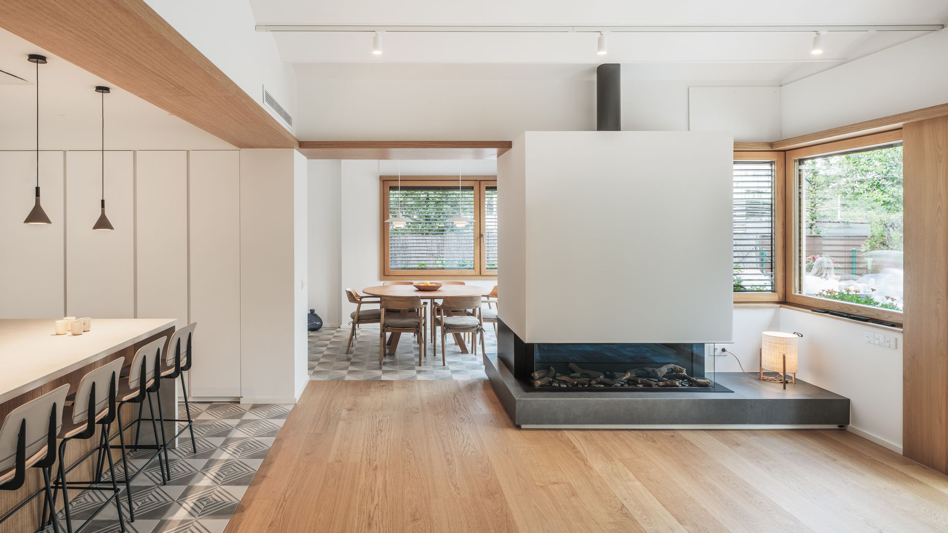 Cocina abierta al salón y al comedor con isla, suelo hidráulico, chimenea, regleta de focos blancos, suelo de madera, taburetes