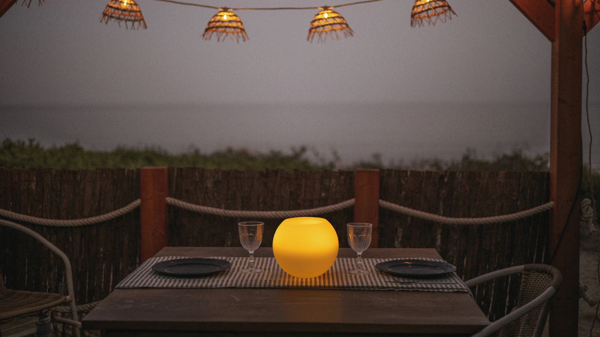 Comedor exterior con pérgola de madera, guirnalda y lámpara de sobremesa