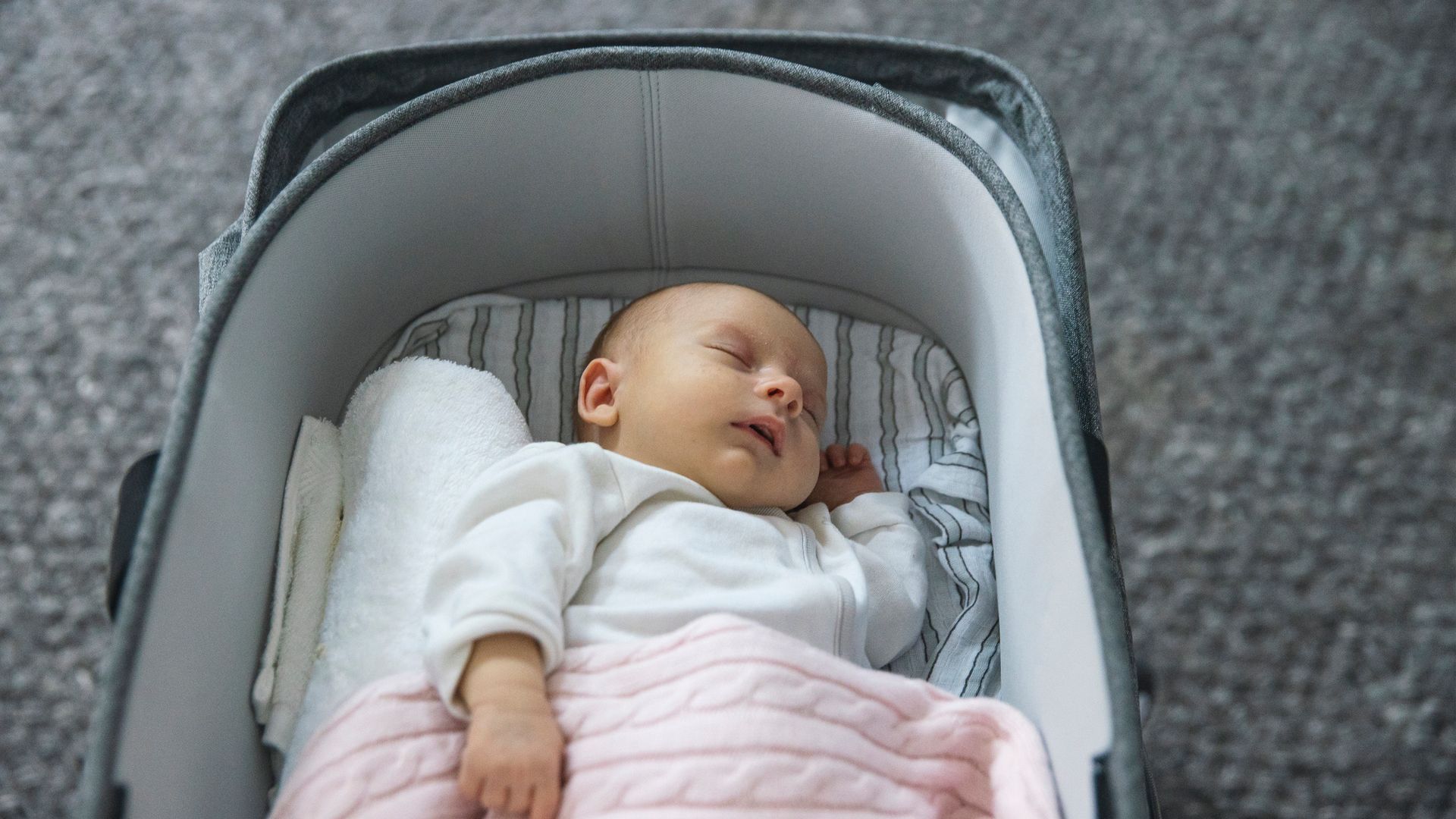 Bebé durmiendo plácidamente en el carrito o capazo sobre una superficie gris.