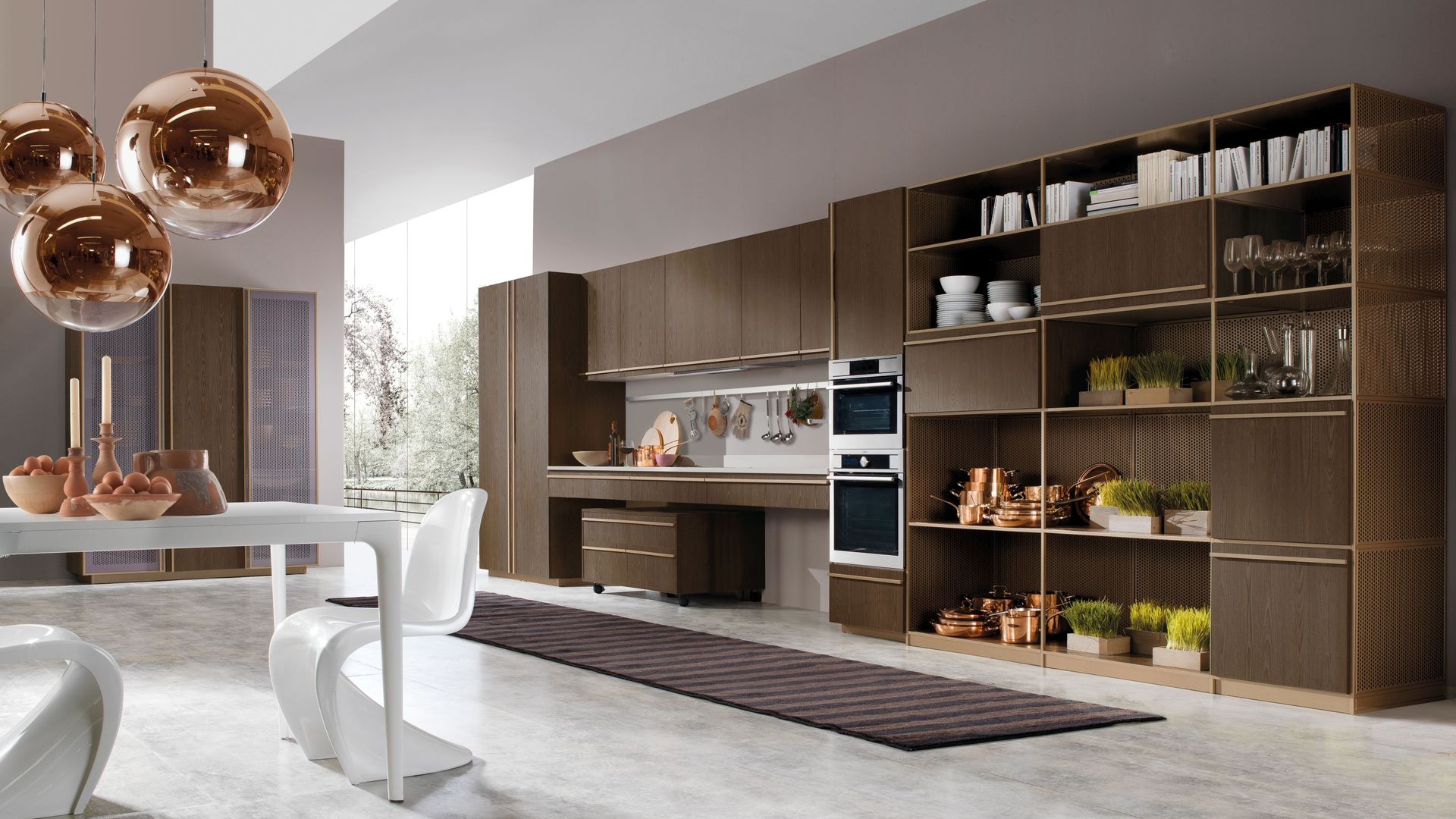 Cocina con un gran frente de armarios, con módulos abierto y cerrados, en color marrón, accesorios de cobre y plantas aromáticas