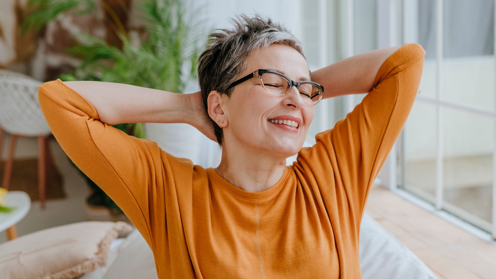 Mujer de 50 años sonriendo y estirándose con los brazos detrás de la cabeza.