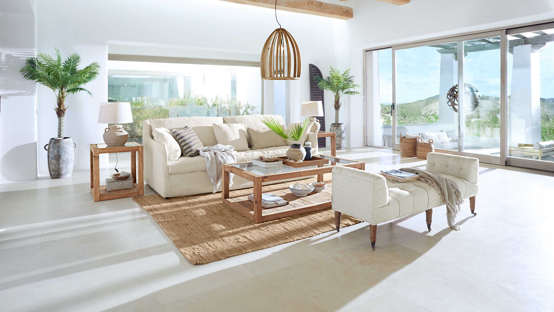 Salón de estilo mediterráneo, con sofá blanco, alfombra de fibras vegetales, lámpara de techo de fibras vegetales, vigas en el techo, chaise longue blanca