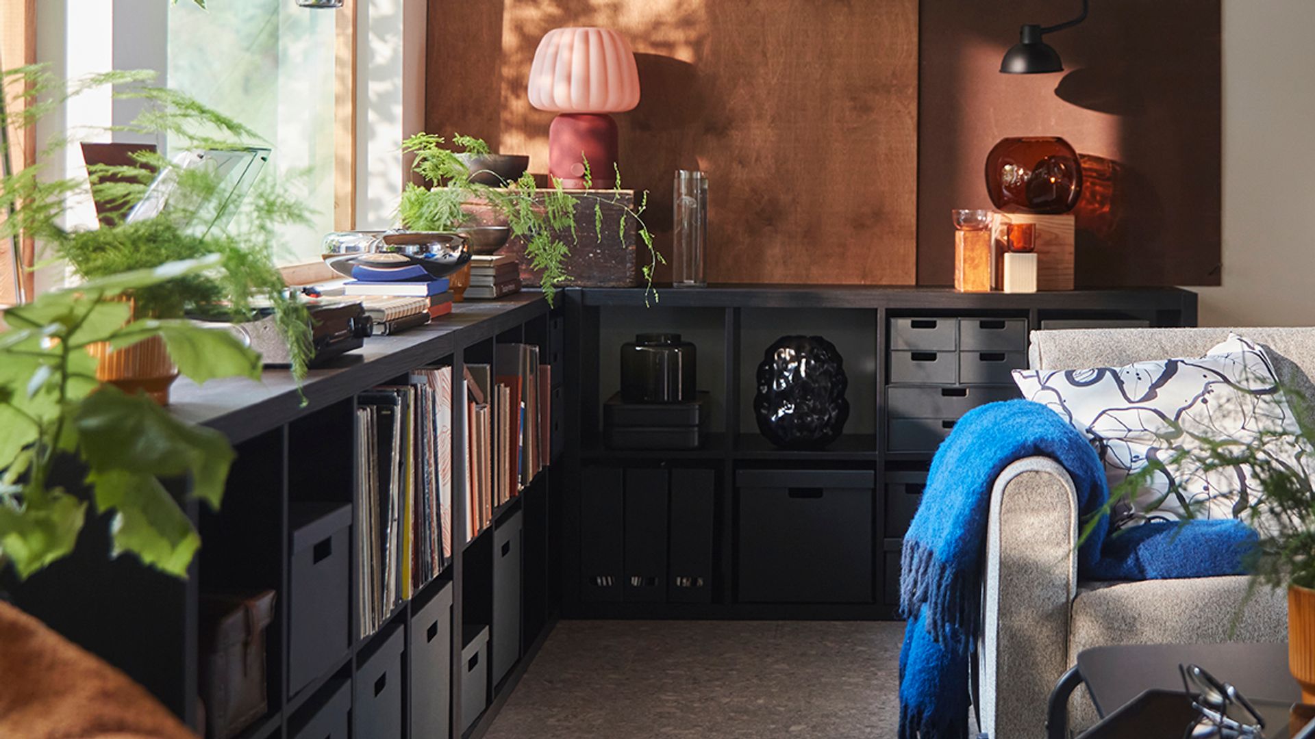 Salón con librería Kallax baja de IKEA de color negro, bajo una ventana con plantas y cestos negros 