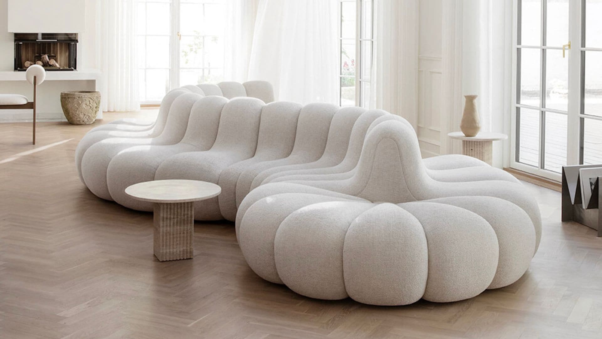 Salón con grandes ventanales con visillos blancos, suelo de madera y sofá XL blanco de formas curvas y orgánicas