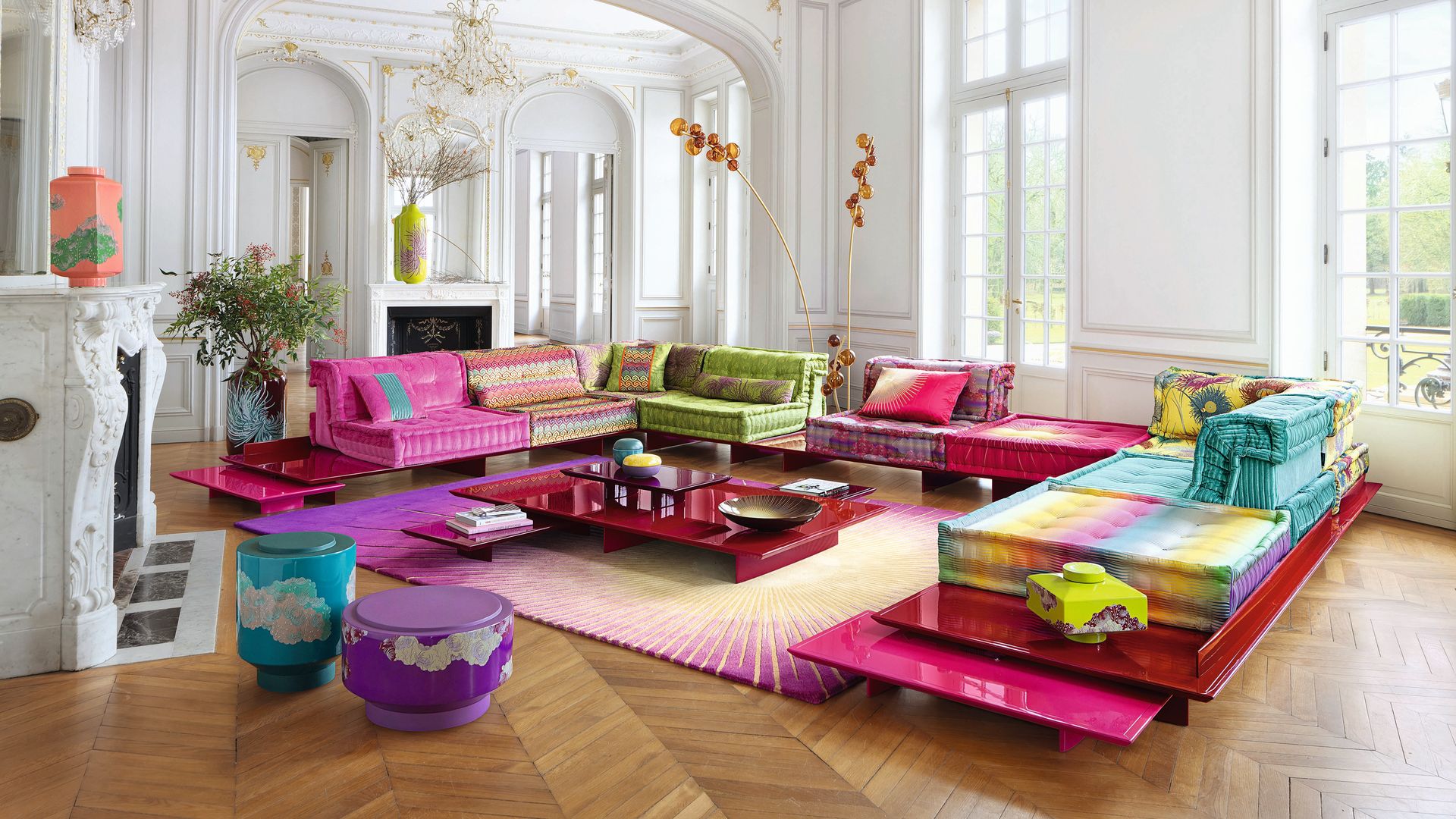 Salón con molduras y lámpara de araña, sofá Mah Jong con telas de Kenzo Takada, mesas de alto brillo en colores rojos y rosas