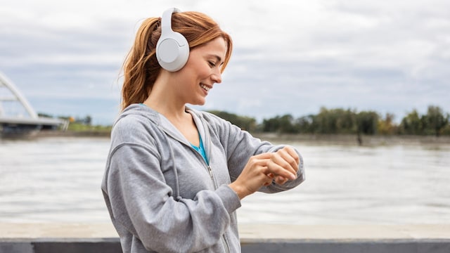Mujer sonriendo mientras prepara su Smartwatch para correr a las orillas del río