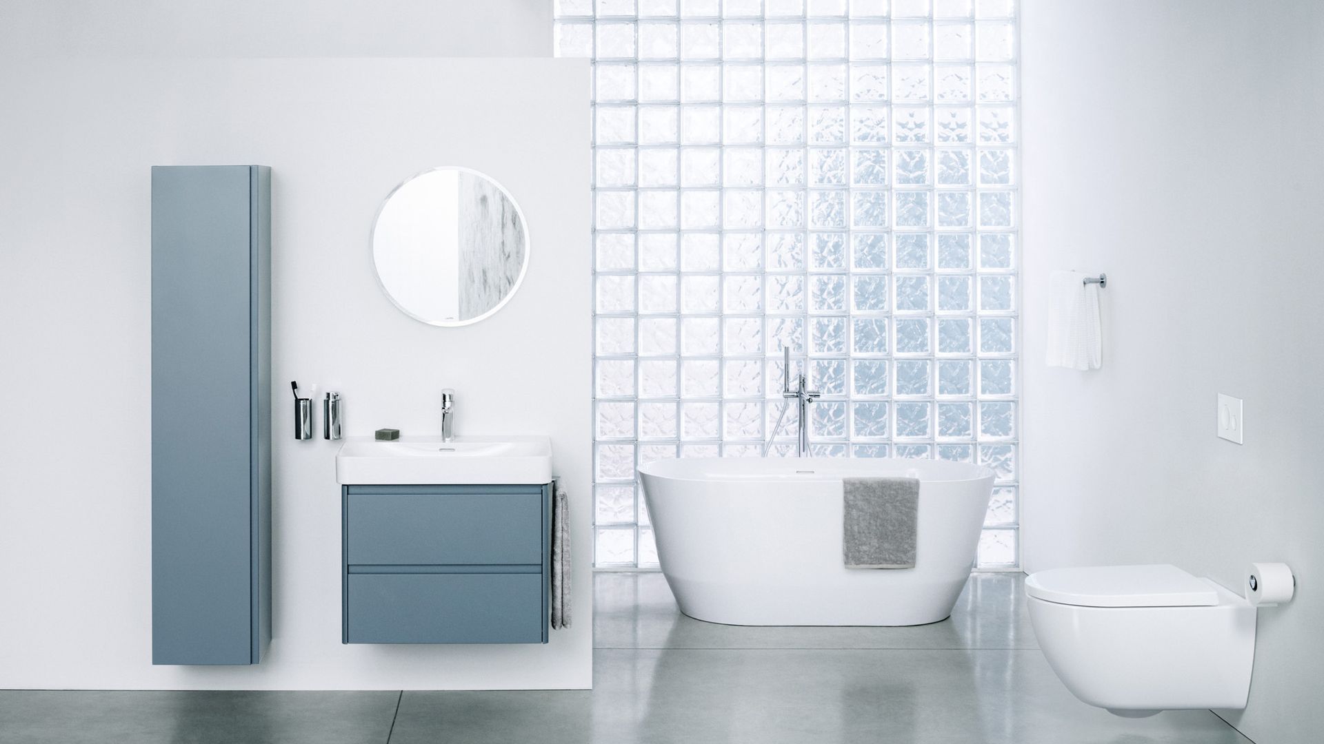 Baño con tabique de pavés, bañera exenta, muebles suspendidos de color azul claro, espejo redondo