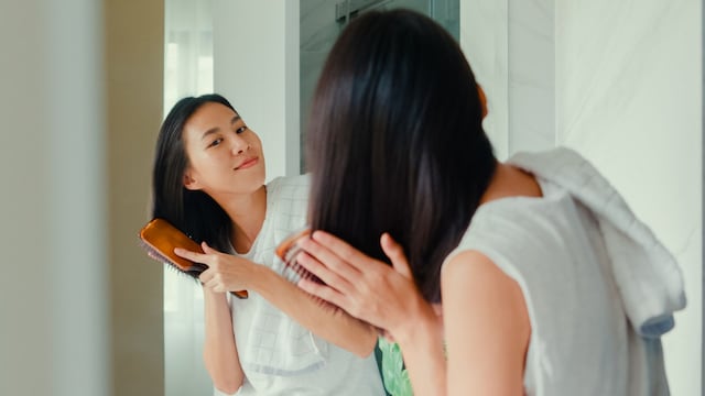 Mujer asiática cepillándose el pelo frente al espejo del baño