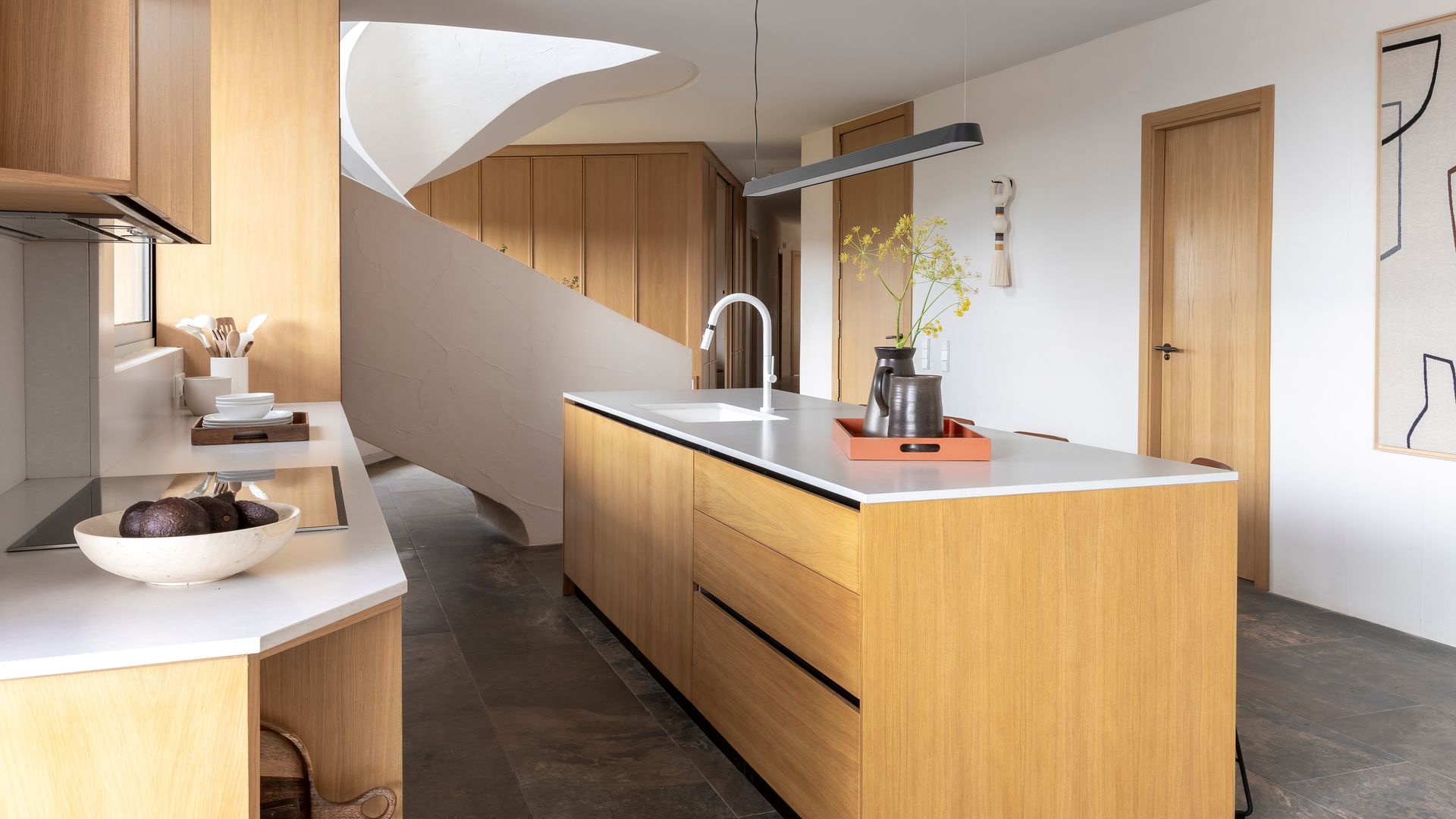 Cocina con isla de madera, abierta con escalera escultura, puertas de madera, suelo porcerlánico