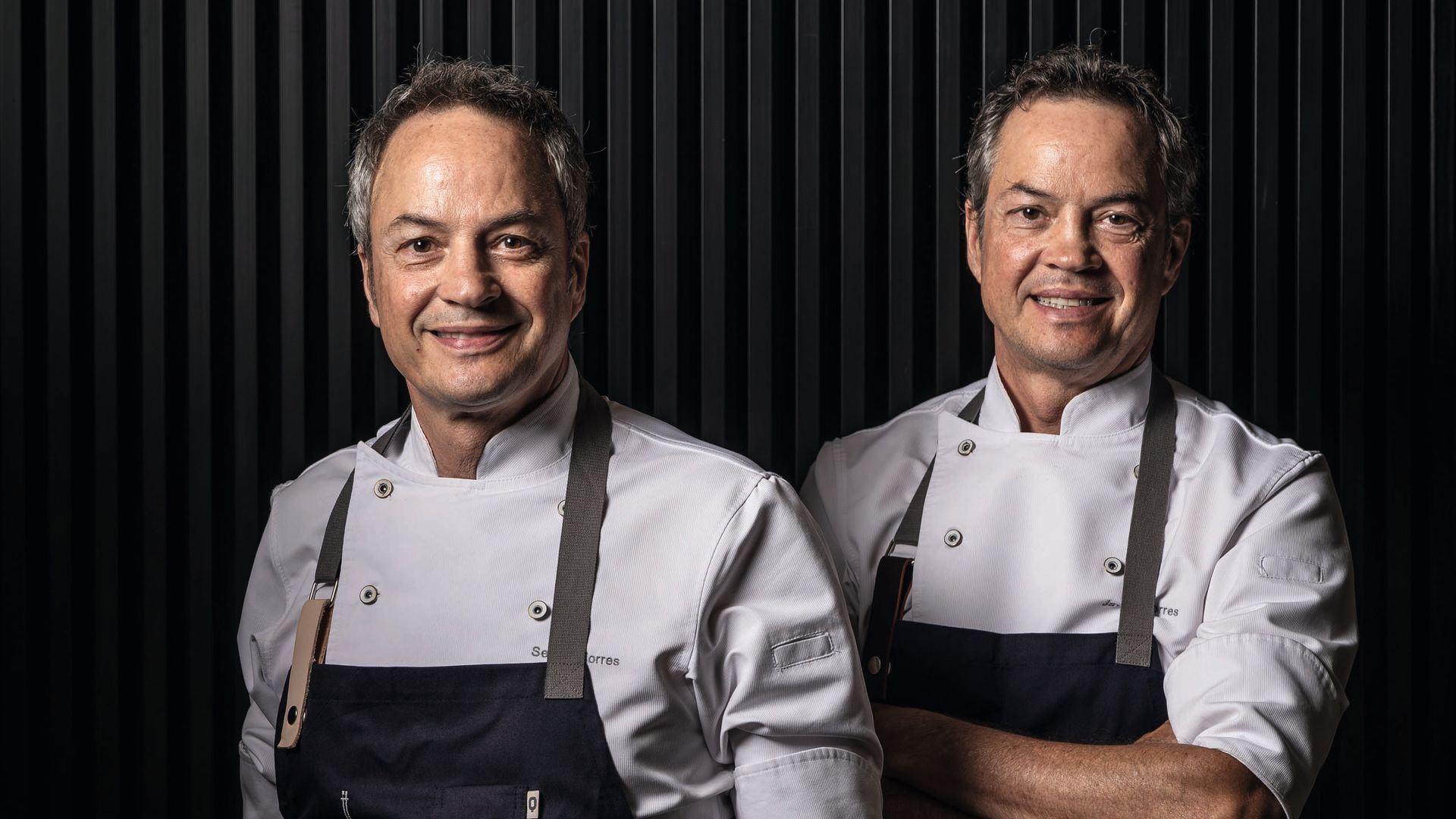 Los Hermanos Torres sonrientes posan juntos, uno con delantal que dice 'COCINA'.