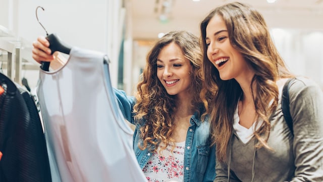 Dos amigas sonrientes de compras mirando una blusa