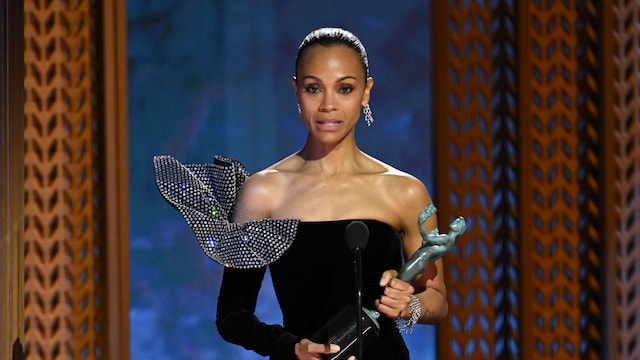 Zoe Saldaña en el escenario sosteniendo su premio SAG Award, vestida elegantemente de negro, durante la ceremonia de premiación.