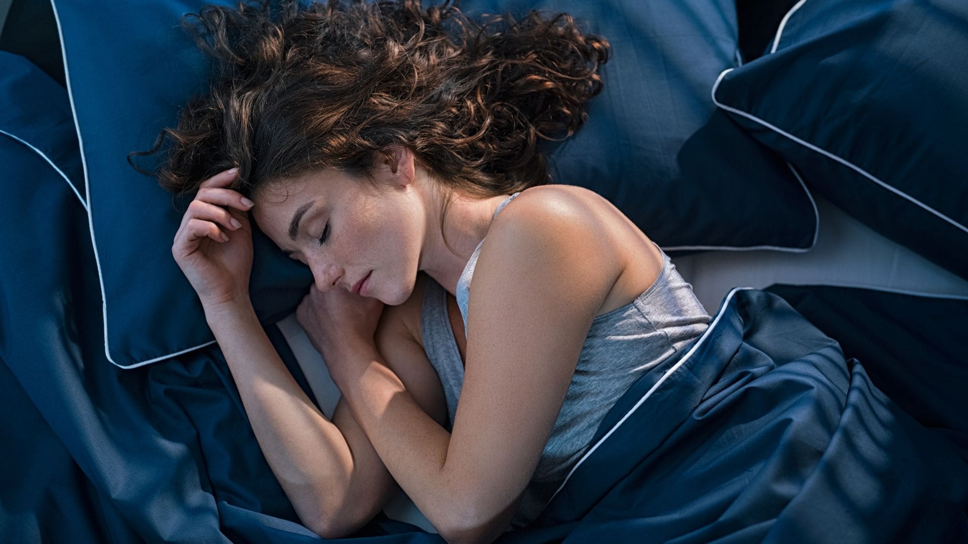 Vista superior de una joven durmiendo de lado en su cama por la noche. Hermosa niña durmiendo profundamente y soñando en casa con una manta azul. Vista en ángulo alto de una mujer dormida con los ojos cerrados.
