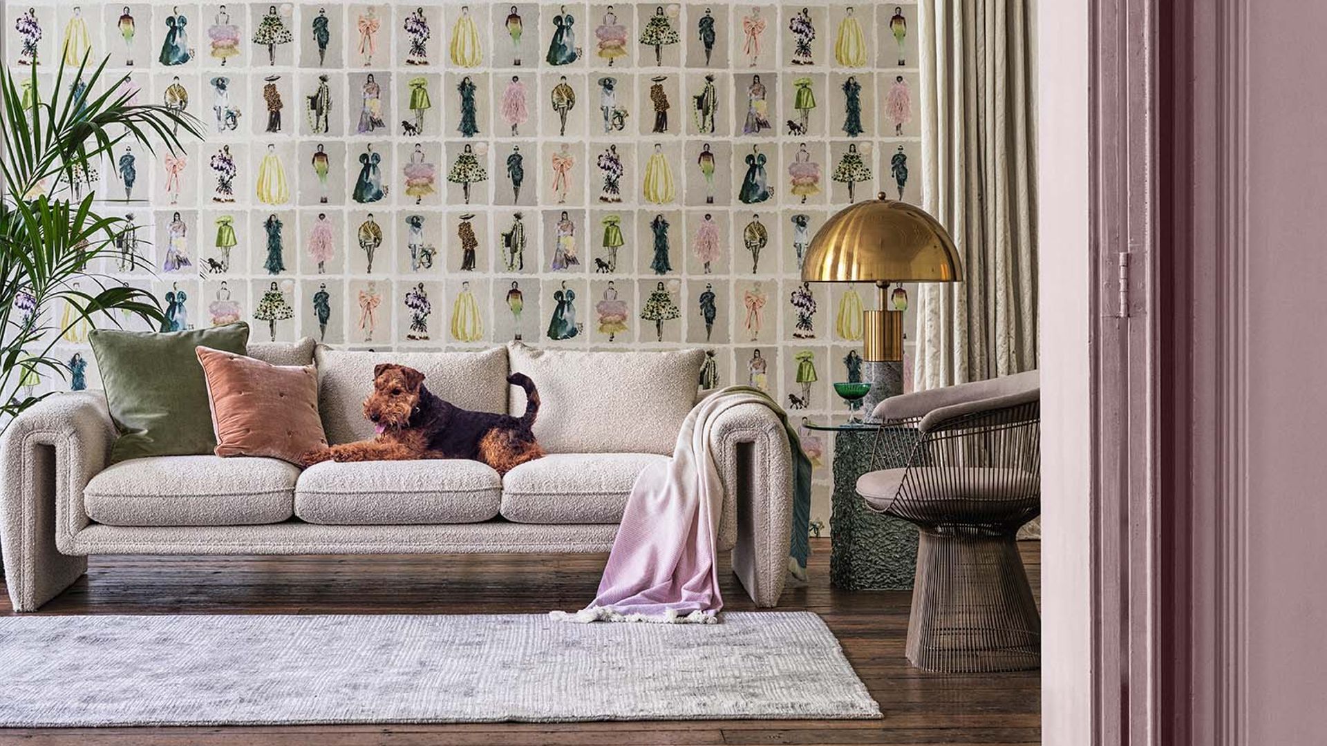 Salón con papel pintado en tonos, rosas, puertas rosas, sofá con perro tumbado, alfombra, lámpara de sobremesa dorada
