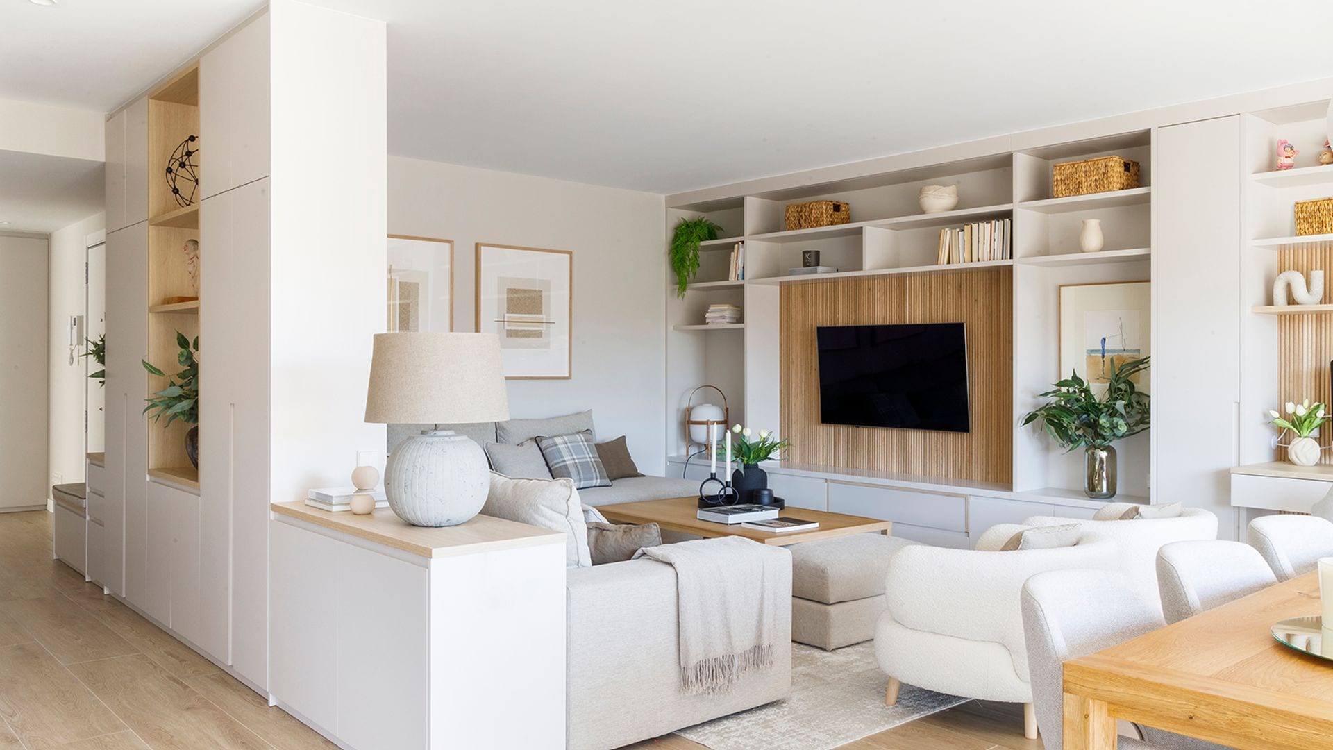 Salón comedor con librería a medida, librería colgada del mueble, sofás blancos, alfombra, estantería abierta blanca a modo de tabique, que separa la estancia del recibidor 