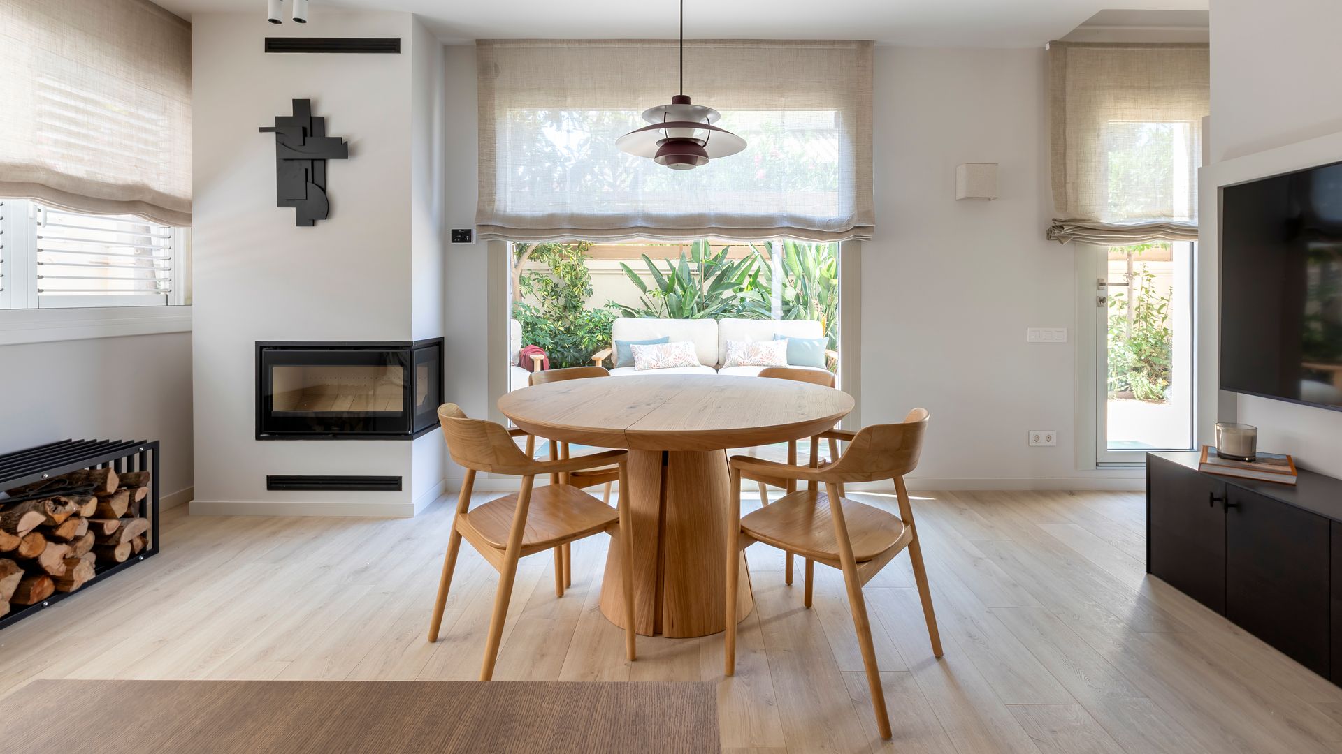 Comedor con chimenea, mesa de comedor redonda, mesa de madera, estores lámpara de techo, televisión colgada en la pared 