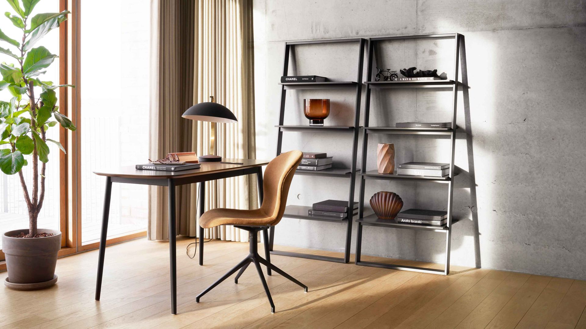 Despacho con ventana, estanterías negras iguales, suelo de madera, mesa negra, silla, maceta con planta alta y lámpara de sobremesa