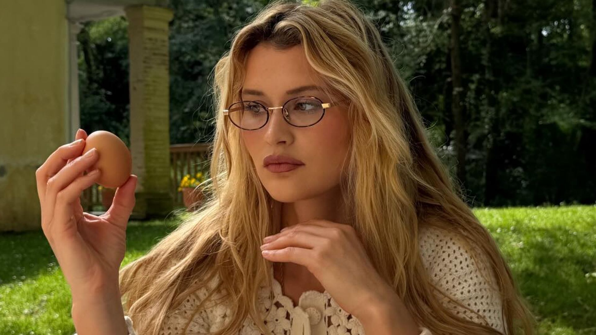 Chloe Lecareuz en el campo con gafas, sujetando un huevo y frente a una mesa de picnic