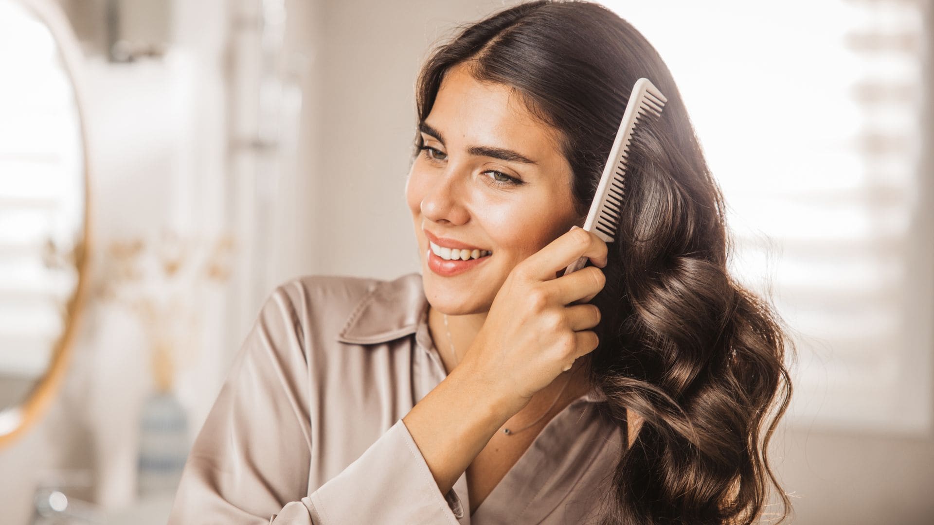 Mujer morena sonriente peinándose el cabello en el cuarto de baño