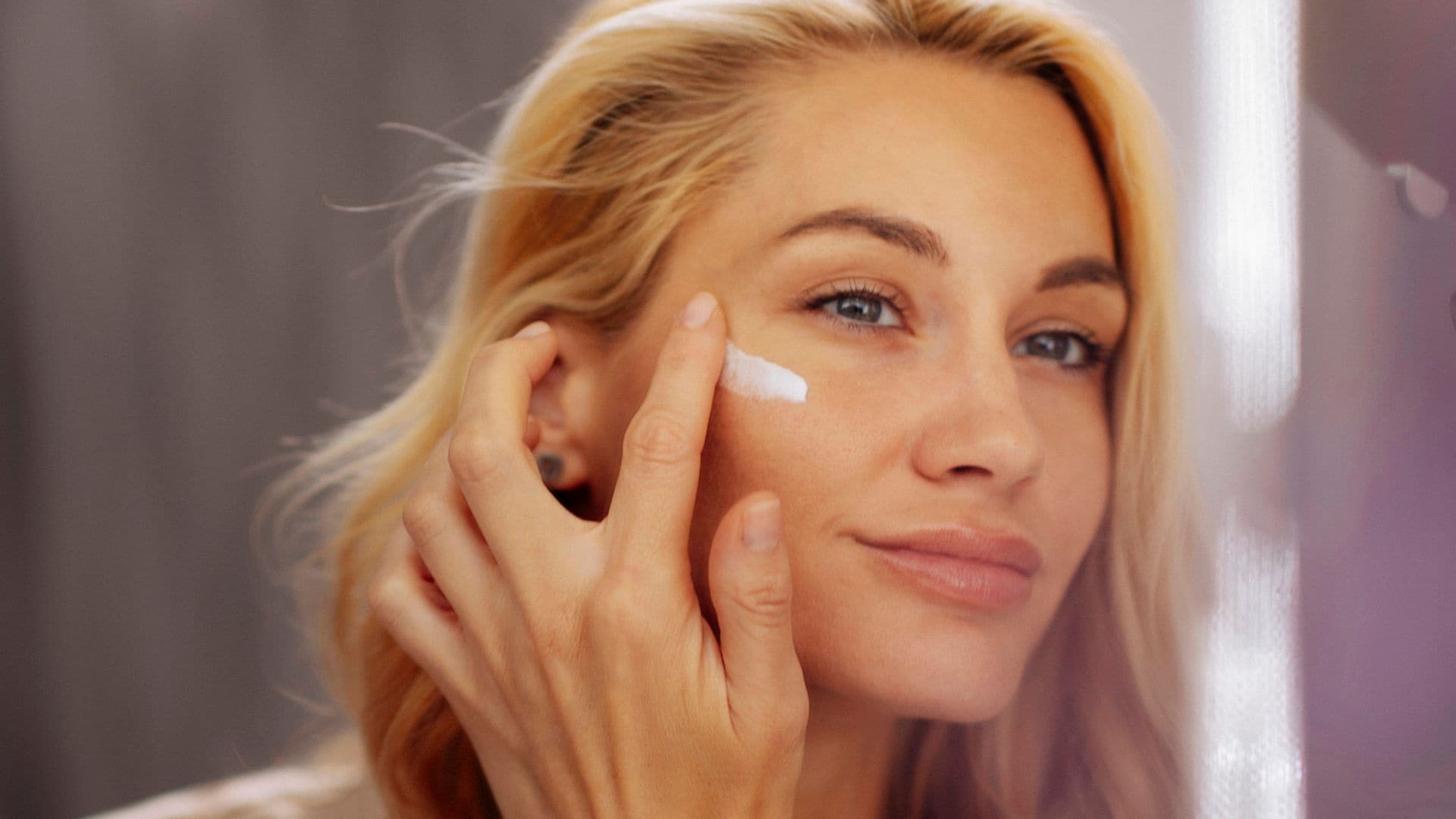 Mujer rubia aplicándose crema frente al espejo