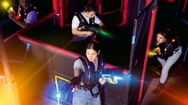 Jóvenes jugando con pistolas láser de colores en una habitación oscura
