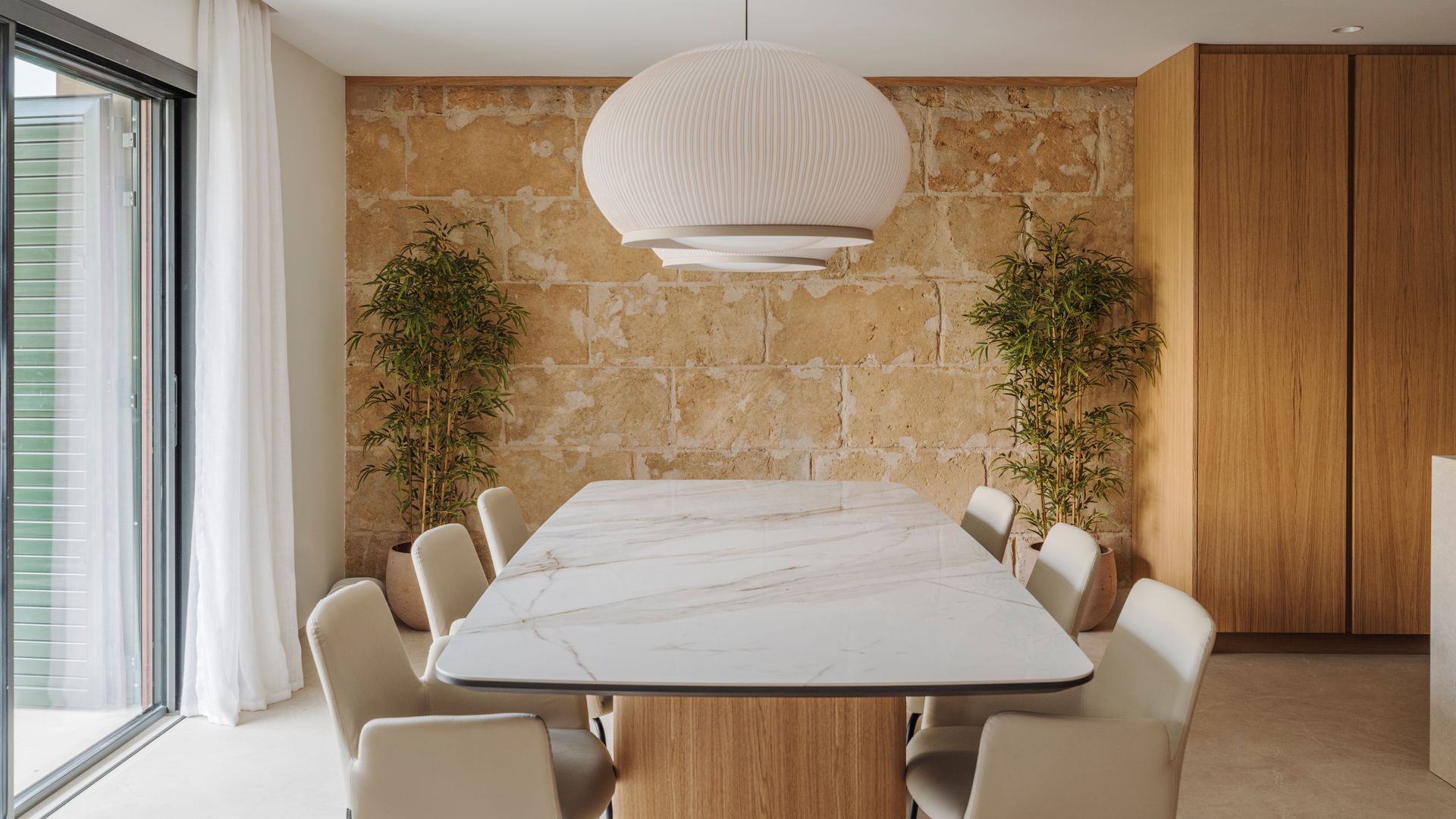 Comedor con mesa extragrande para ocho comensales, pared de piedra natural, sillas tapizadas, lámparas de techo