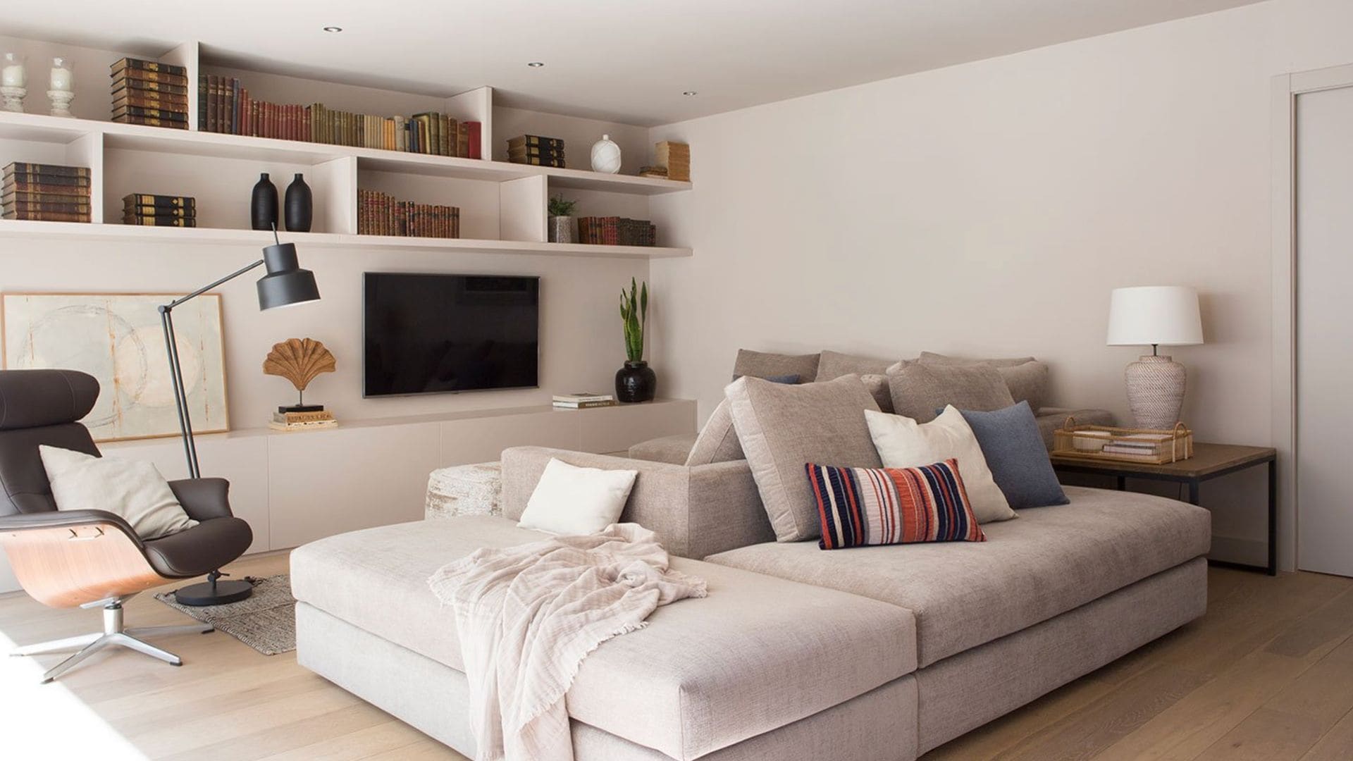 Salón con sofá modular, estantería a medida blanca, televisión colgada en la pared, lámpara de pie negra, lámpara de sobremesa blanca