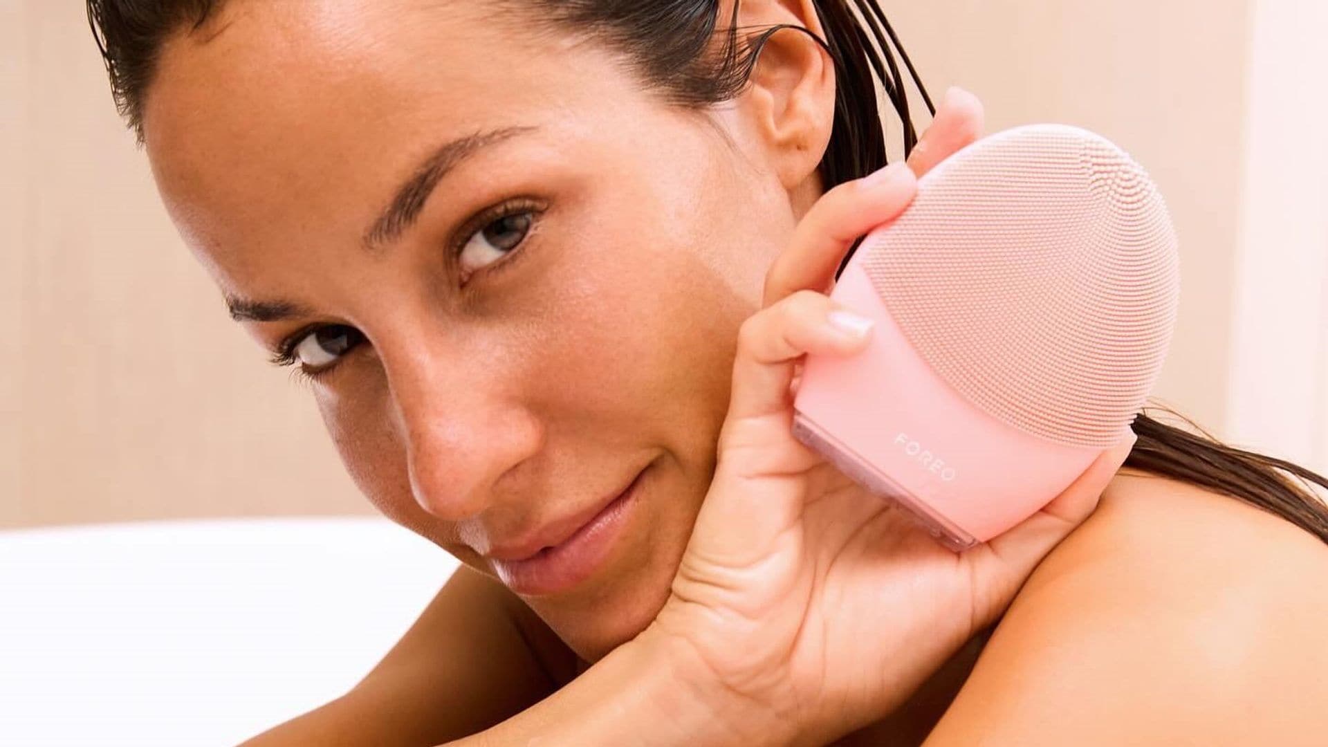 Mujer en la bañera mirando a cámara con cepillo limpiador facial de FOREO en la mano