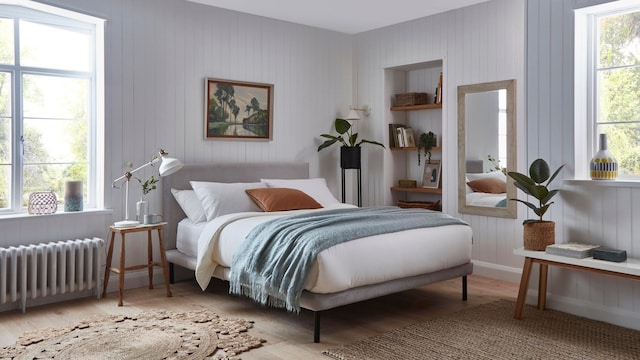 Dormitorio con paredes blancas, hornacina con baldas de madera, alfombra de fibras vegetales, grandes ventanales, plantas, espejo, cuadro y banco de madera