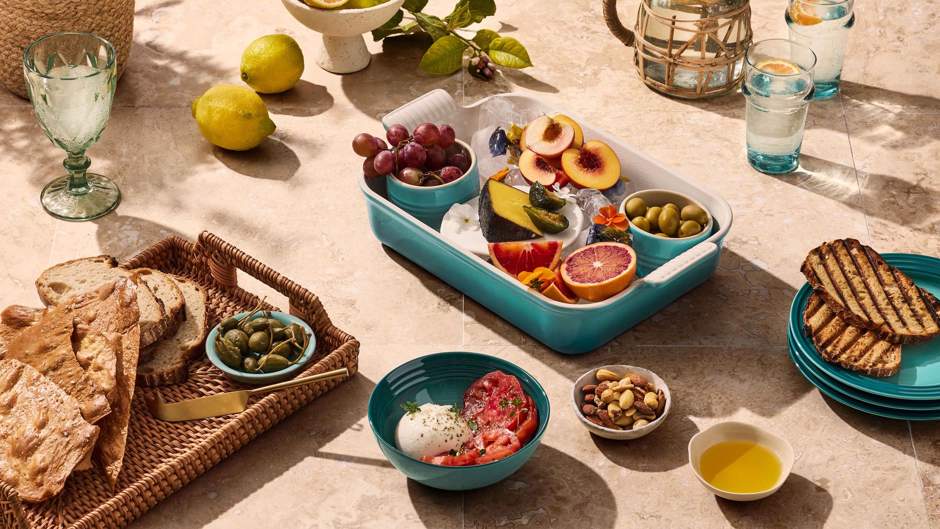 Mesa de verano con bandejas, fuentes y cuencos de Le Creuset en color azul, bandeja de fibras vegetales para el pan 