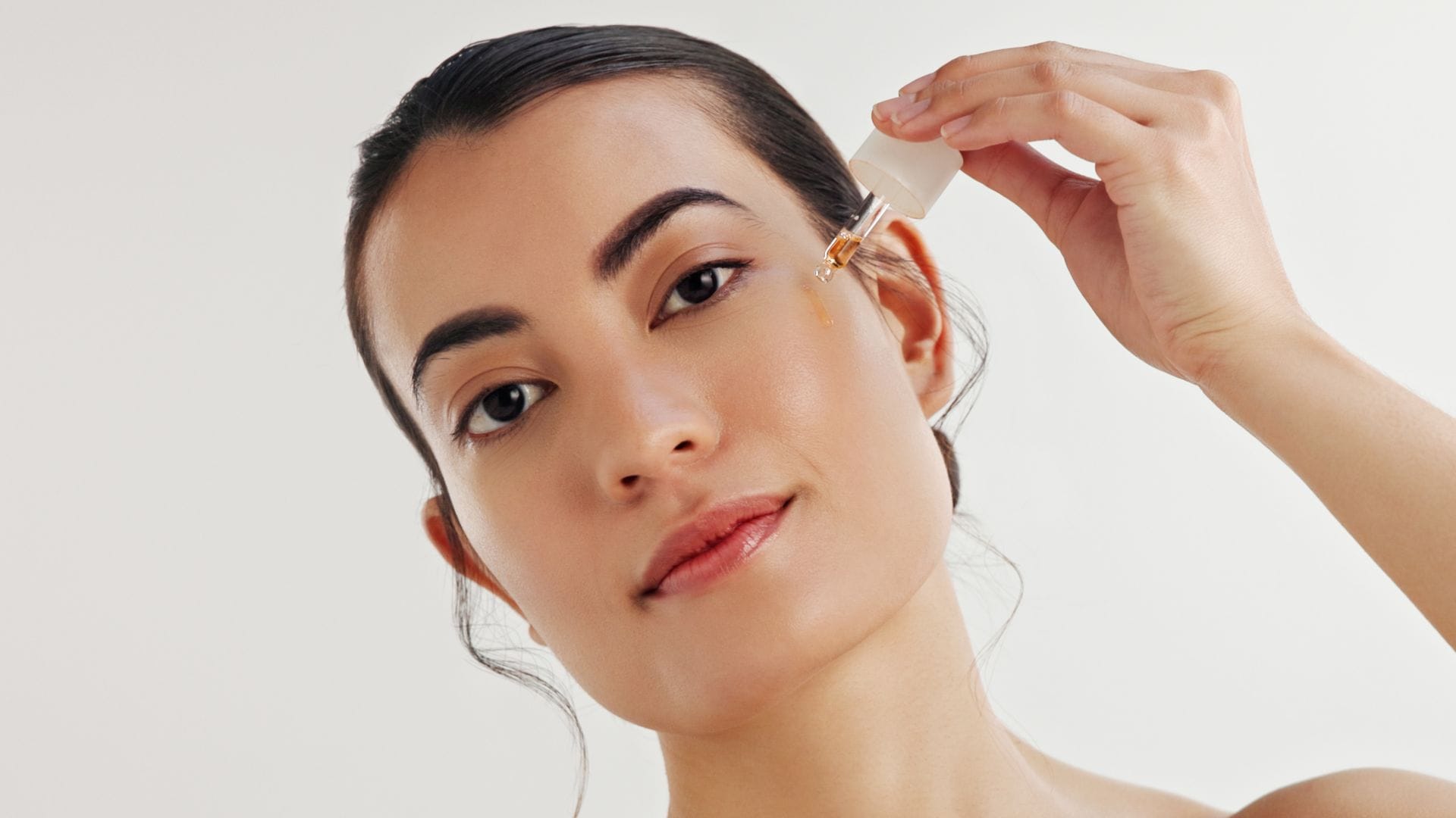 Mujer joven aplicándose sérum facial anaranjado en el rostro