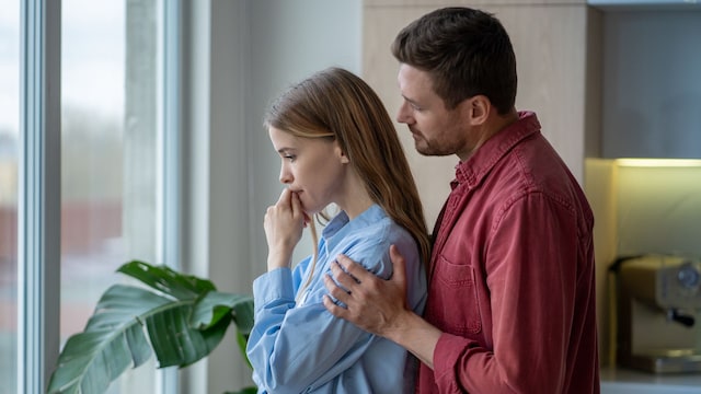 pareja consolando a su mujer, junto a la ventana de su casa