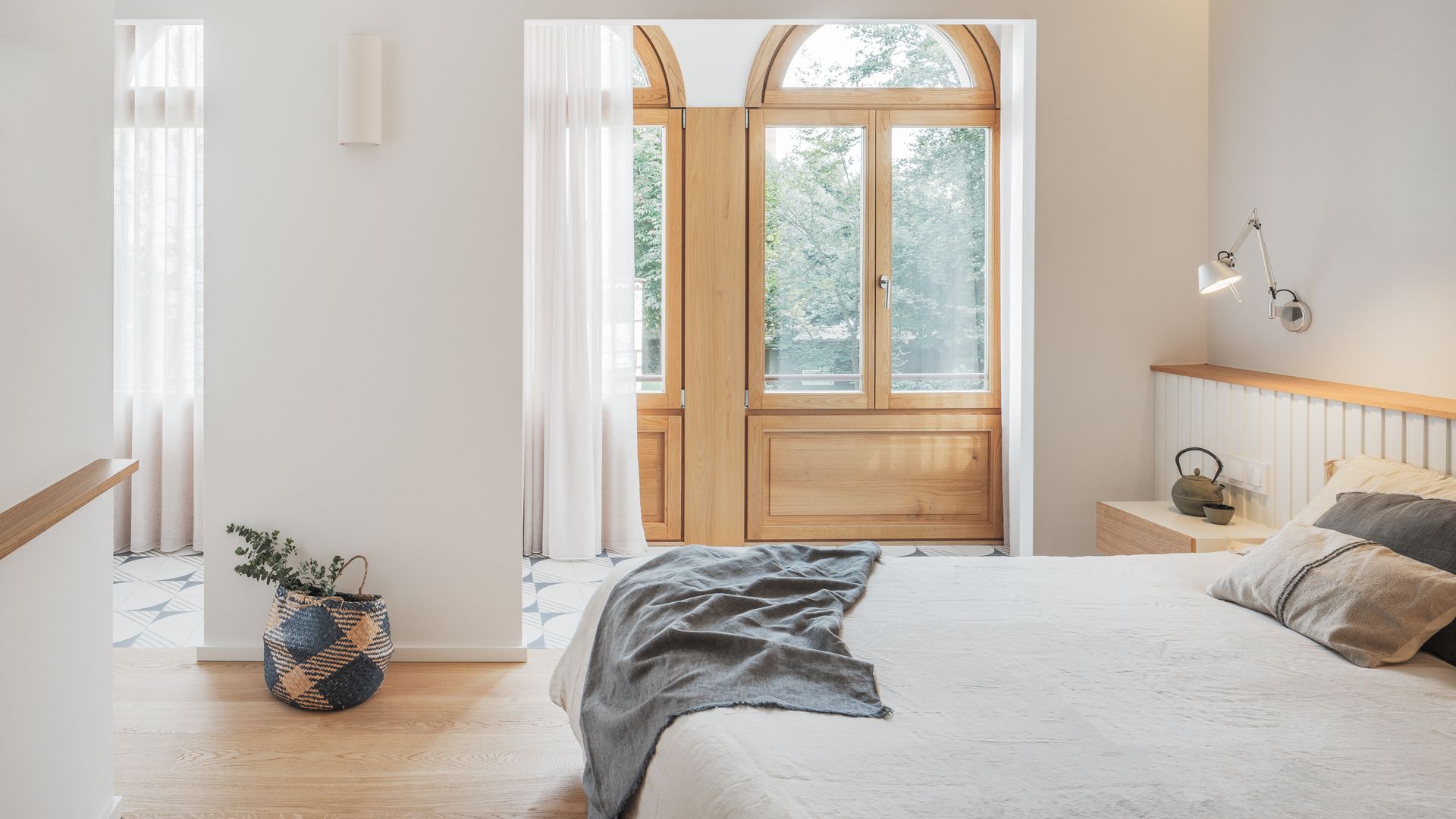 Dormitorio con galería con ventanas con arcos de madera, suelo de madera, cabecero con repisa de madera, cortinas blancas