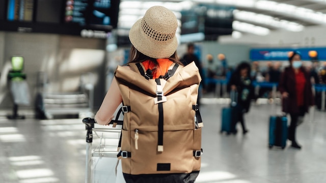 Mujer en el aeropuerto mirando las pantallas de salida, con una mochila a la espalda.
