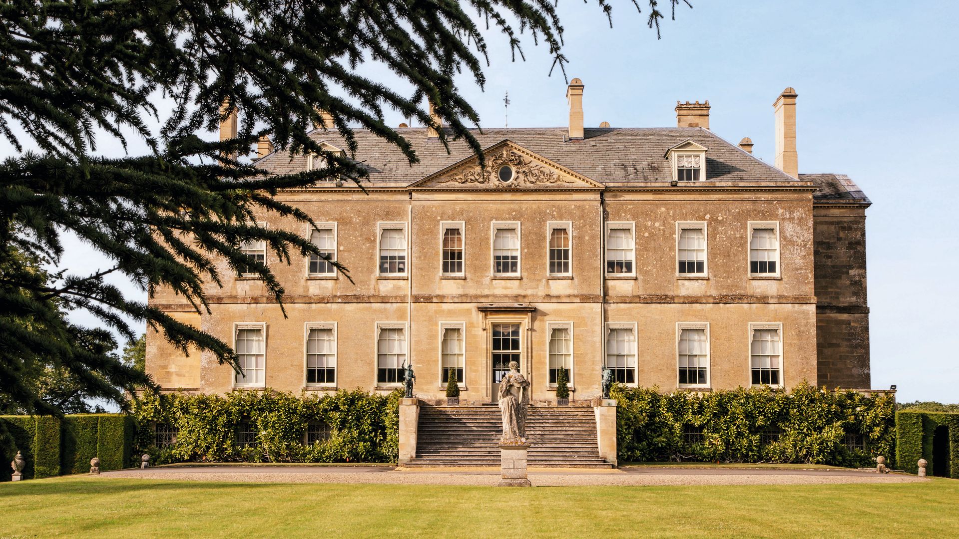 Mansión antigua con césped, arbustos y estatua en el frente.