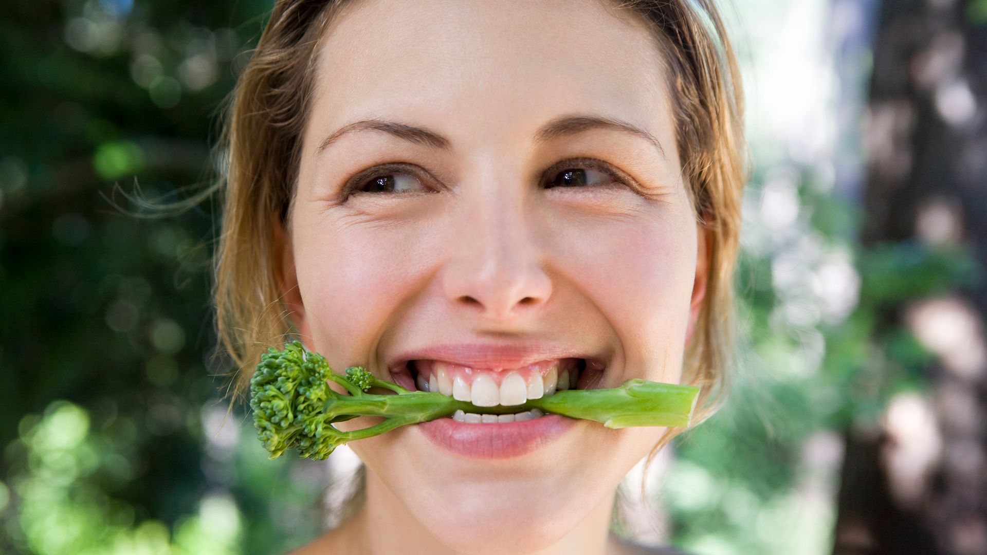 Mujer sonriendo comiendo un brócoli