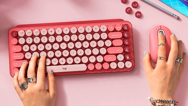 Un teclado rosa de Logitech sobre una mesa rosa y una chica usándolo