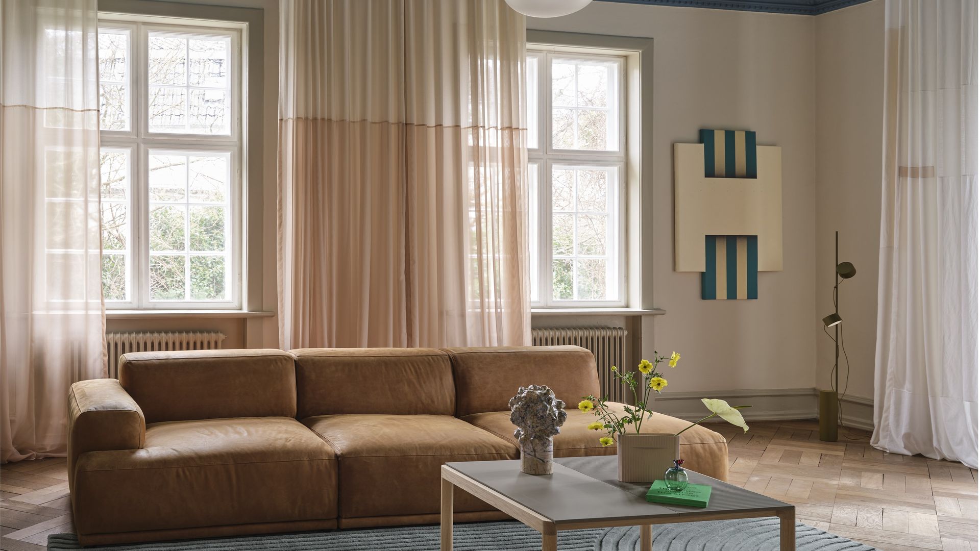 Salón con sofá marrón, alfombra, mesa de centro, lámpara de techo blanca, ventanas con radiadores, cortinas, techo azul 